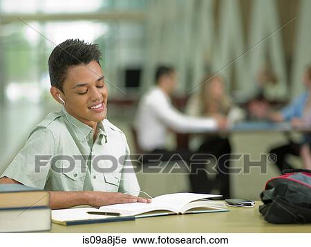 Stock Image - Young student wearing earphones and looking at school books. Fotosearch