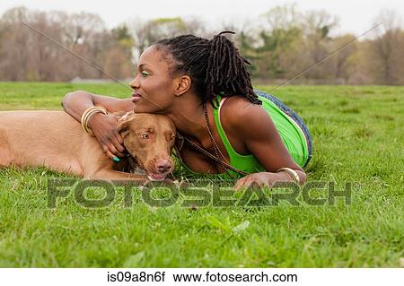 Stock Image - Young woman and her dog lying on grass. Fotosearch