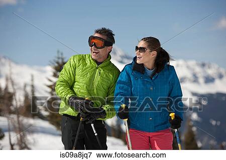 Stock Photo - Young woman and mature man in skiwear holding ski poles. Fotosearch