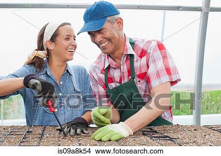 Picture - Young woman and mature man planting seeds in garden centre, portrait. Fotosearch