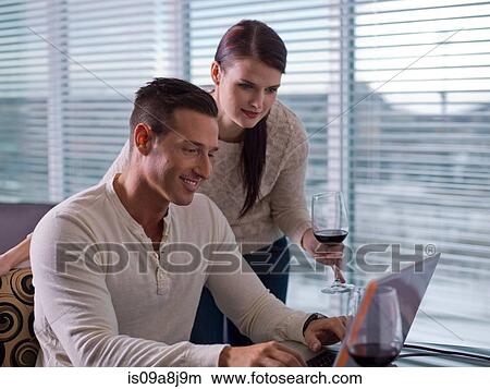 Young woman and mid adult man enjoyng wine and using laptop View Large Photo Image Picture - Young woman and mid adult man enjoyng wine and using laptop. Fotosearch
