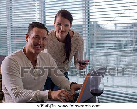 Young woman and mid adult man enjoyng wine and using laptop, portrait View Large Photo Image Picture - Young woman and mid adult man enjoyng wine and using laptop, portrait. Fotosearch