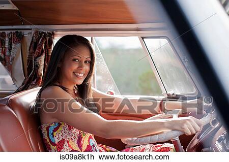 Stock Image - Young woman driving camper van and smiling, portrait. Fotosearch