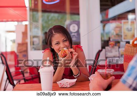 Stock Photo - Young woman eating hotdog in diner, portrait. Fotosearch