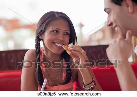 Stock Photograph - Young woman eating with boyfriend in diner, smiling. Fotosearch