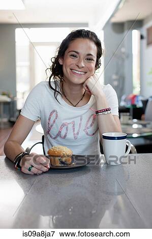 Stock Photo - Young woman enjoying coffee and muffin in kitchen, portrait. Fotosearch