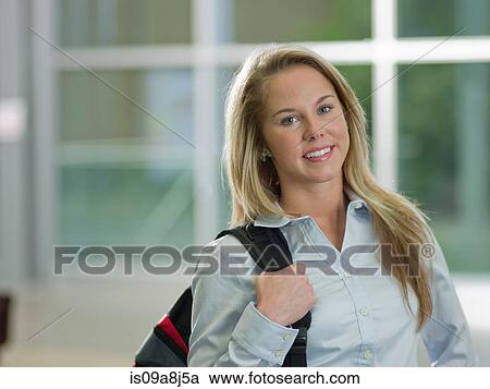 Stock Image - Young woman holding backpack smiling, portrait. Fotosearch