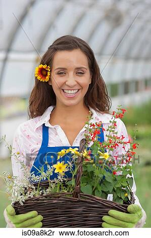 Stock Photography - Young woman holding basket of flowers in garden centre, portrait. Fotosearch