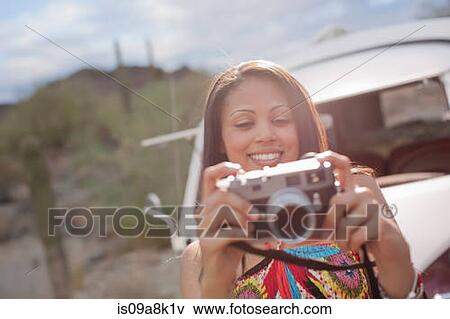 Young woman holding camera on road trip, smiling View Large Photo Image Stock Photo - Young woman holding camera on road trip, smiling. Fotosearch