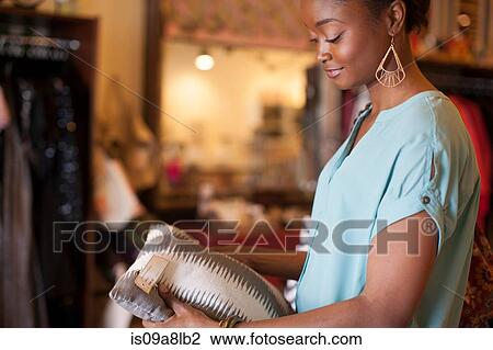 Stock Image - Young woman holding cushion in vintage shop. Fotosearch