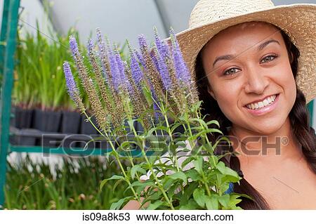 Stock Image - Young woman holding flowers in garden centre, portrait. Fotosearch