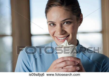 Stock Photograph - Young woman holding hot drink indoors, close up. Fotosearch