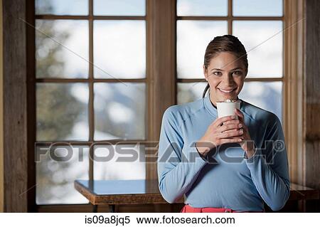 Stock Photography - Young woman holding hot drink indoors. Fotosearch