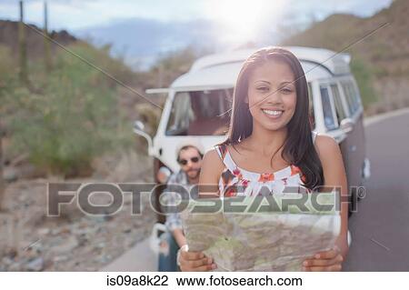 Stock Image - Young woman holding map on road trip, smiling. Fotosearch