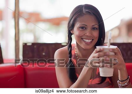 Picture - Young woman holding milkshake in diner, smiling. Fotosearch