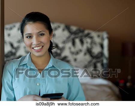 Stock Image - Young woman holding mobile phone and smiling, portrait. Fotosearch