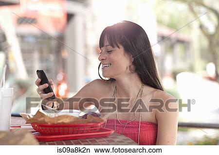 Young woman holding mobile phone in outdoor cafe, smiling View Large Photo Image Picture - Young woman holding mobile phone in outdoor cafe, smiling. Fotosearch