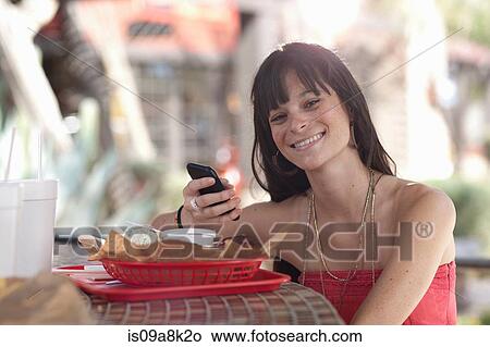 Young woman holding mobile phone in outdoor cafe, portrait View Large Photo Image Picture - Young woman holding mobile phone in outdoor cafe, portrait. Fotosearch