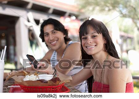 Young woman holding mobile phone in outdoor cafe, smiling View Large Photo Image Stock Image - Young woman holding mobile phone in outdoor cafe, smiling. Fotosearch