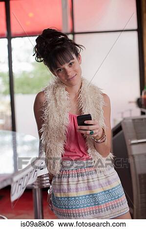 Young woman holding mobile phone in diner, portrait View Large Photo Image Stock Photograph - Young woman holding mobile phone in diner, portrait. Fotosearch