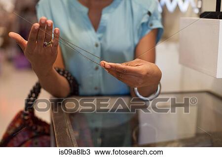 Stock Image - Young woman holding necklace in vintage shop. Fotosearch
