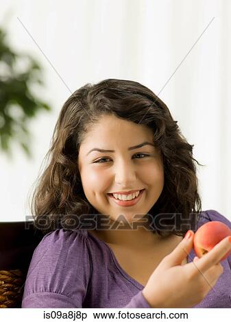 Stock Photography - Young woman holding peach, smiling. Fotosearch