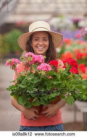 Stock Image - Young woman holding plants in garden centre, portrait. Fotosearch