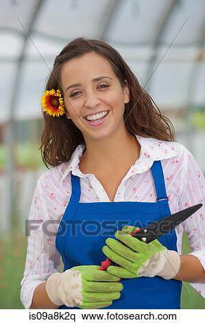 Stock Photography - Young woman holding pruning shears in garden centre, portrait. Fotosearch