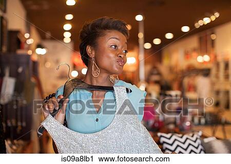 Stock Image - Young woman holding silver top in vintage shop, pouting. Fotosearch
