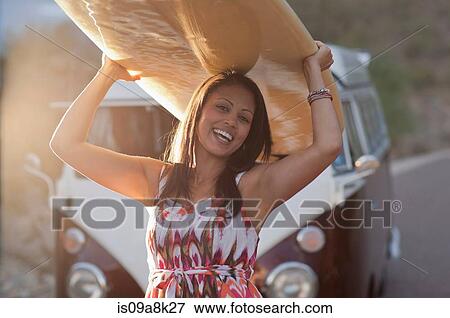 Young woman holding surfboard on road trip, smiling View Large Photo Image Stock Photo - Young woman holding surfboard on road trip, smiling. Fotosearch