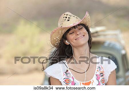 Young woman in cowboy hat wearing earphones, smiling View Large Photo Image Picture - Young woman in cowboy hat wearing earphones, smiling. Fotosearch