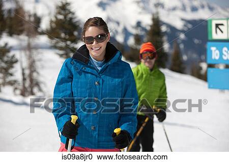 Stock Image - Young woman in skiwear holding ski poles, portrait. Fotosearch