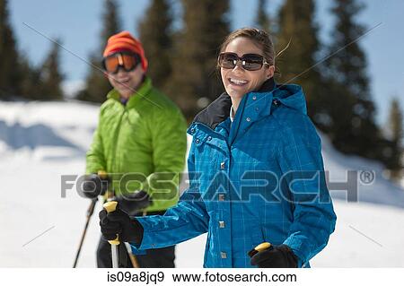 Stock Photo - Young woman in skiwear holding ski poles, portrait. Fotosearch