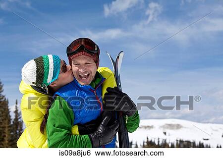 Stock Photograph - Young woman in skiwear kissing mature man holding skis. Fotosearch