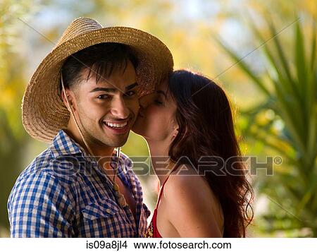 Young woman kissing man wearing sun hat, smiling View Large Photo Image Picture - Young woman kissing man wearing sun hat, smiling. Fotosearch