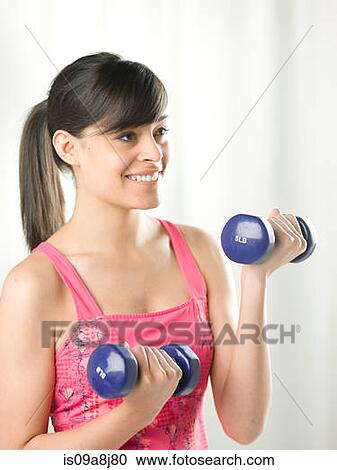 Young woman lifting dumb bells, smiling View Large Photo Image Stock Image - Young woman lifting dumb bells, smiling. Fotosearch