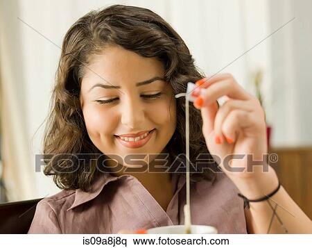Stock Photography - Young woman lifting teabag from cup, smiling. Fotosearch