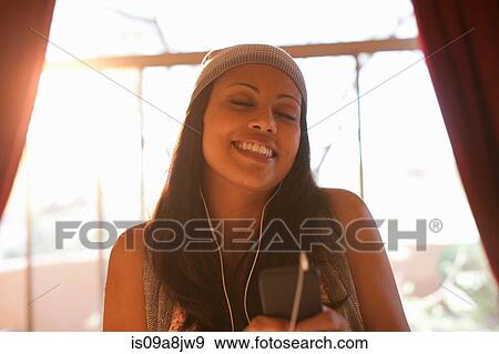Stock Photo - Young woman listening to mp3 player in hotel room, eyes closed. Fotosearch