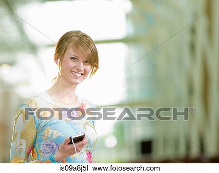 Stock Image - Young woman listening to music with mp3 player, portrait. Fotosearch