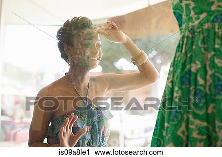 Stock Image - Young woman looking at dress through shop window. Fotosearch