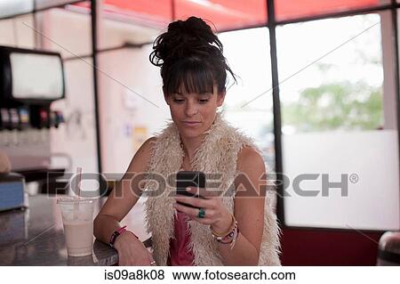Stock Photo - Young woman looking at mobile phone in diner. Fotosearch