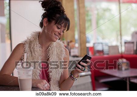 Stock Photo - Young woman looking at mobile phone in diner. Fotosearch