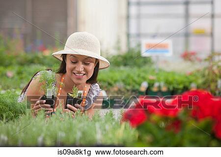 Young woman looking at plants in garden centre, smiling View Large Photo Image Stock Image - Young woman looking at plants in garden centre, smiling. Fotosearch