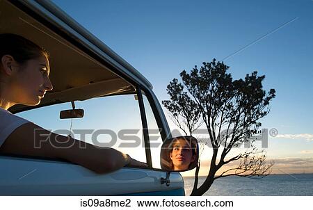 Stock Image - Young woman looking out of camper van window at dusk. Fotosearch