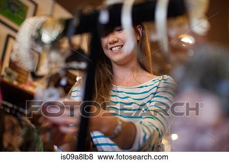 Stock Photo - Young woman looking through clothes rail in vintage shop. Fotosearch