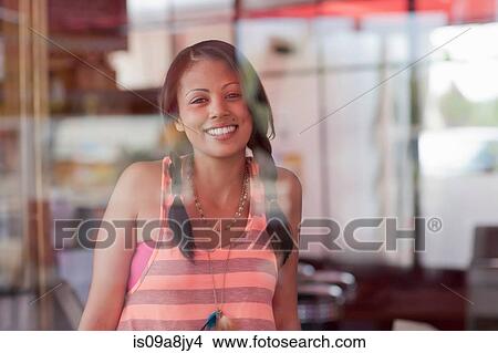Picture - Young woman looking through window of diner, portrait. Fotosearch