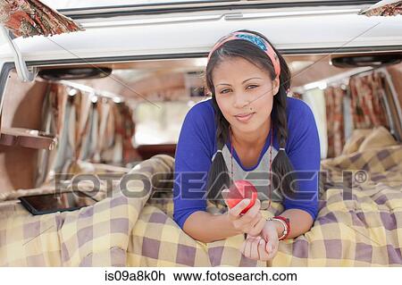 Stock Image - Young woman lying in camper van, smiling. Fotosearch