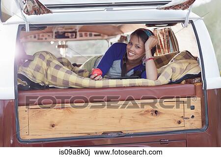 Stock Image - Young woman lying in camper van, smiling. Fotosearch