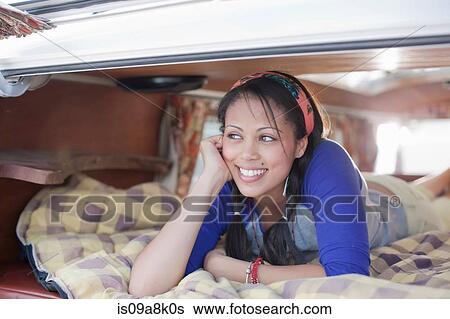 Stock Photograph - Young woman lying in the back of camper van, smiling. Fotosearch
