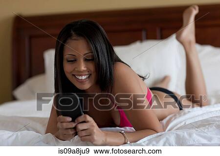 Young woman lying on bed in underwear looking at cellphone View Large Photo Image Stock Photo - Young woman lying on bed in underwear looking at cellphone. Fotosearch